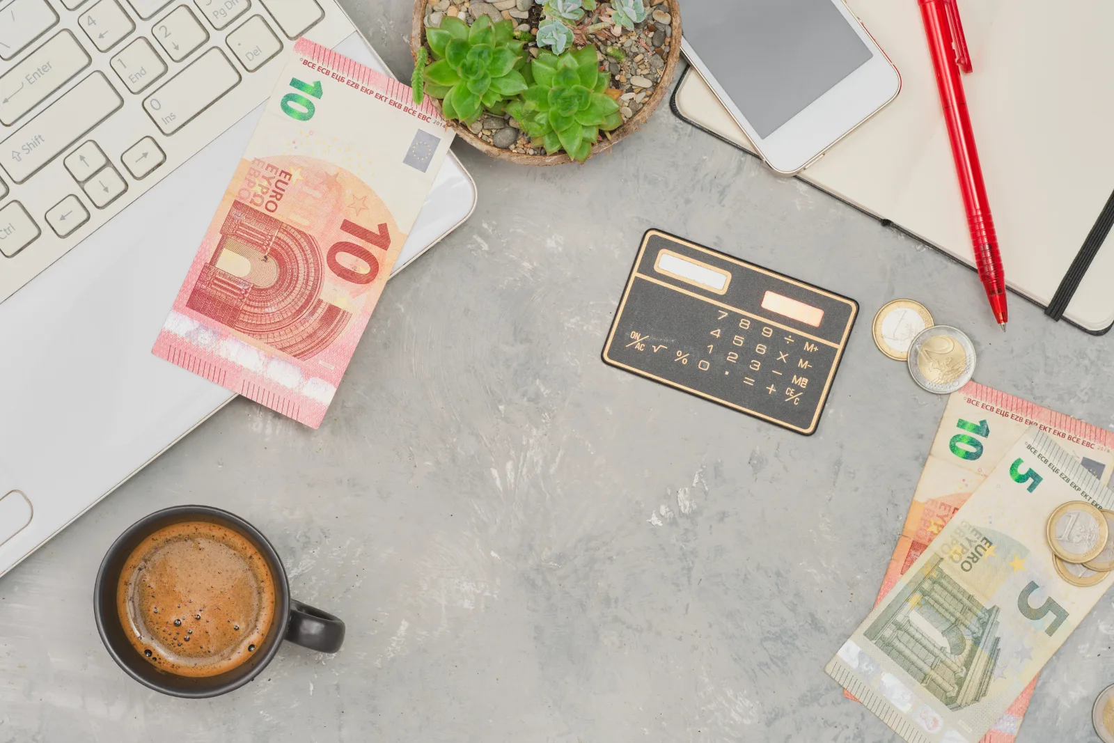 Schreibtisch mit Euro-Scheinen, Taschenrechner, Kaffee und Notebook