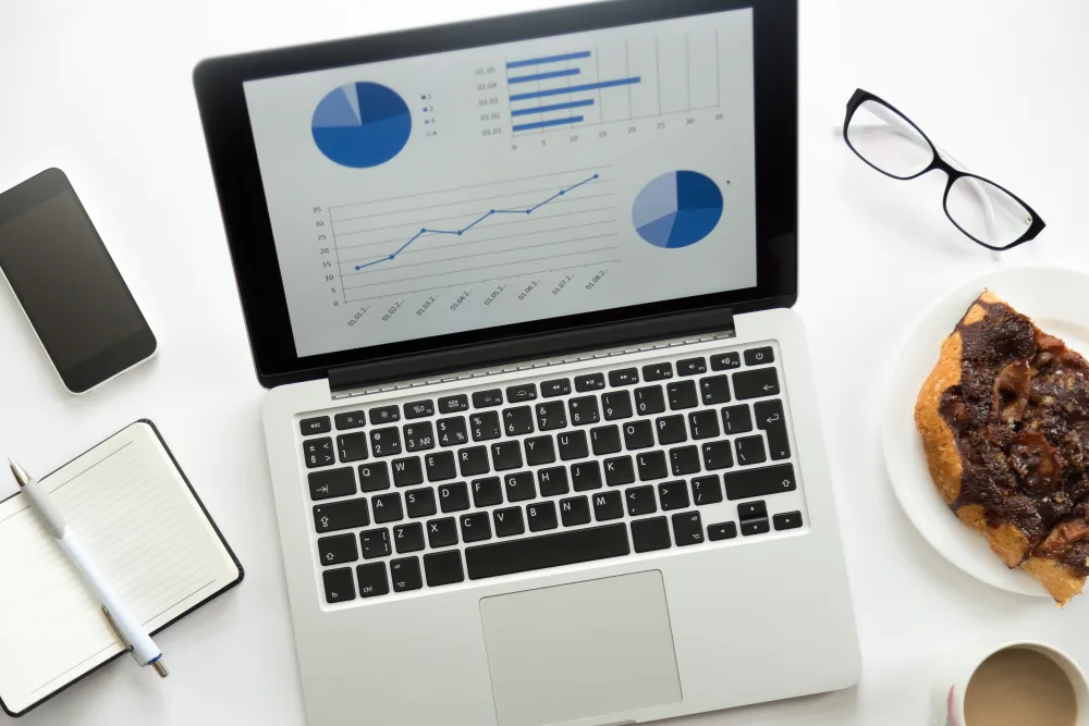 Aufgeklapptes Notebook mit Diagrammen, Brille und Notizblock von oben
