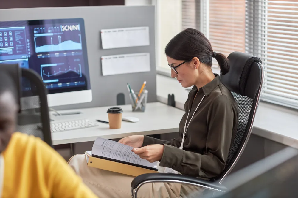 Person liest Dokumentation am Schreibtisch neben einem Monitor
